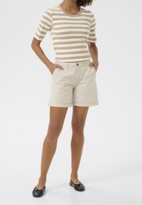 Raitattu vaaleanbeige ja valkoinen ribbimekko, yhdistettynä vaaleanbeigeihin shortseihin, joissa on käännetyt lahkeet ja perinteiset taskut. Mustat tasapohjaiset kengät täydentävät asua.