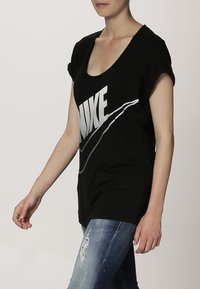 Svart kortärmad t-shirt med en stor vit "NIKE" logotyp och swoosh-grafik över framsidan. Mjuk, lätt tyg. Avslappnad passform.
