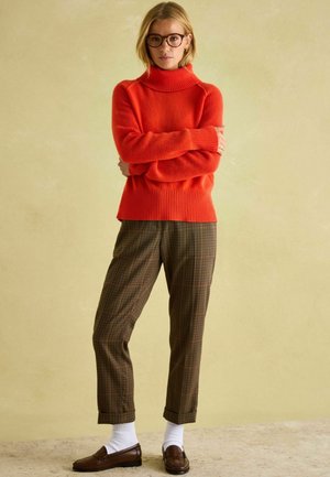 Red wool turtleneck sweater with ribbed texture, paired with brown plaid trousers. Brown loafers and white socks complete the outfit.