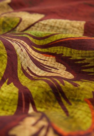 Tissu multicolore avec un motif floral présentant des verts, des rouges et des bruns. La texture semble lisse avec un léger éclat.