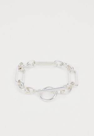 Silver chain bracelet with interlocking oval and rectangular links. Features a toggle closure with a circular accent. Smooth, shiny metal finish.