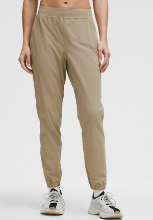 Light beige, lightweight athletic pants with an elastic waistband and cuffs. Smooth texture, tapered fit, and functional design.