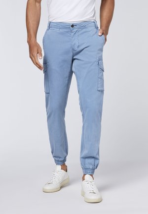 Helle blaue Cargo-Hosen mit elastischen Bündchen, mehreren Seitentaschen und einer glatten Baumwolltextur. Kombiniert mit weißen Sneakers.