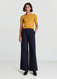 Pull à manches courtes moutarde associé à un pantalon large marine. Texture lisse, détail côtelé subtil sur le pull et accent bouton sur le pantalon.