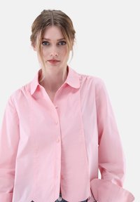 Pink cotton button-up shirt with a collared neckline, front placket, puffed sleeves, and subtle texture, displaying a relaxed fit.