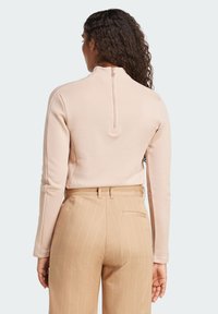 Ljust rosa långärmad topp med hög hals och dragkedjedetalj på ryggen, kombinerad med beige randiga byxor. Slät tyg och åtsittande design.