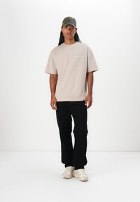 Beige oversized t-shirt med hvid tekst, sorte tapered bukser og cremede sneakers. Kappen har kamuflage-mønster med et grønt og gråt design.