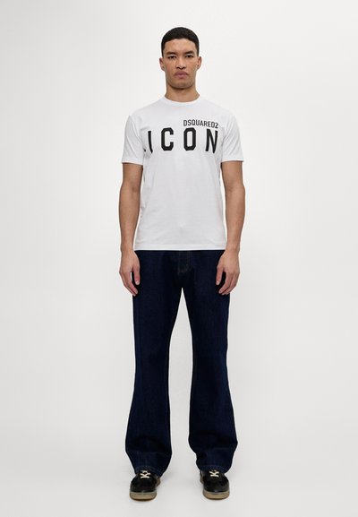 White cotton t-shirt featuring bold black text "ICON" on the front, paired with dark blue wide-leg jeans and black sneakers.