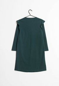Vestido verde oscuro con mangas largas, de forma sencilla y con acentos de volantes en los hombros. Hecho de una tela suave, con un dobladillo recto.