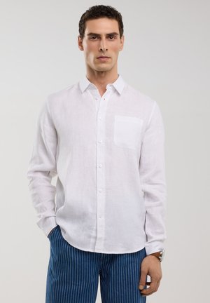 Chemise en lin blanche à boutonnière, avec une poche poitrine unique et des manches longues, associée à un pantalon bleu à rayures.