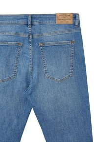 Jean en denim bleu clair avec taille mi-haute, deux poches arrière, coutures contrastées et étiquette en cuir beige cousue à la taille.