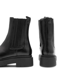 Melnas ādas Čelsi kurpes ar elastīgām sānu paneļiem, masīviem zoliem un nelielām zīmola logo augšējās ārējās malās.