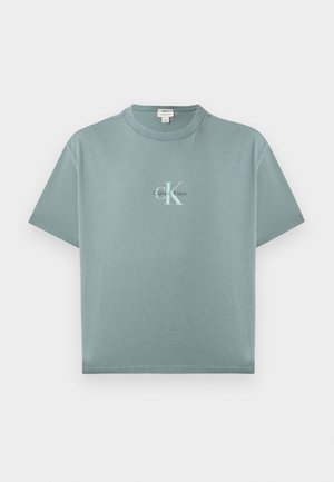 T-shirt à manches courtes bleu sarcelle clair avec col rond, logo Calvin Klein centré en texte blanc et noir sur le devant.