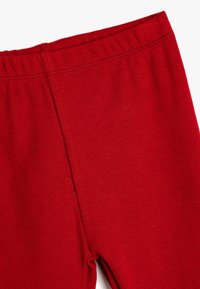 Czerwone legginsy prążkowane z szerokim elastycznym pasem, charakteryzujące się gładką teksturą i aerodynamicznym designem. Zbliżenie ukazujące detale tkaniny.