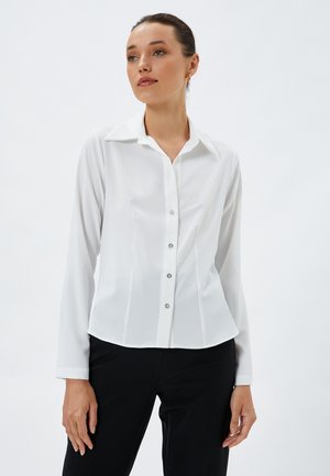 Weiße Bluse mit langen Ärmeln und klassischem Kragen, vorderer Knopfverschluss mit silberfarbenen Knöpfen und taillierter Passform. Glatte Stofftextur.