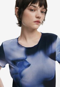 Sleek, fitted top in translucent fabric with a blue gradient, featuring a ribbed texture and a rounded neckline with contrasting trim.