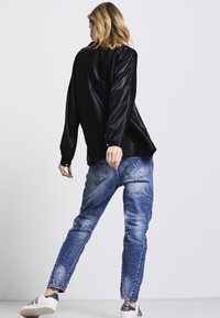 Schwarzes, glänzendes Langarmshirt kombiniert mit hellblauen, ausgewaschenen Jeans. Die Schuhe sind weiß mit metallischen Akzenten.
