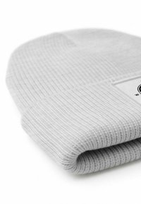 Gray ribbed knit beanie with a folded cuff and a small label tag. Soft texture, cylindrical shape, and even stitching throughout.