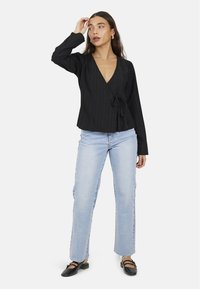 Blusa nera avvolgente con righe verticali, maniche lunghe e dettaglio con fiocco. Abbinata a jeans azzurri dritti e ballerine nere.