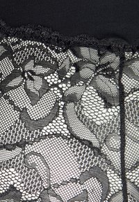 Tela de encaje negra con patrones florales y un borde festoneado, combinada con un panel negro sólido en la parte superior para contraste y textura.