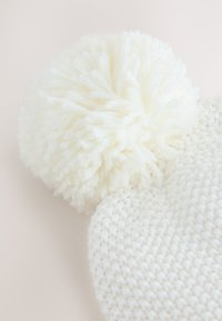 Witte gebreide muts met een gestructureerd patroon en een pluizige pompon bovenop, gemaakt van zachte wol.