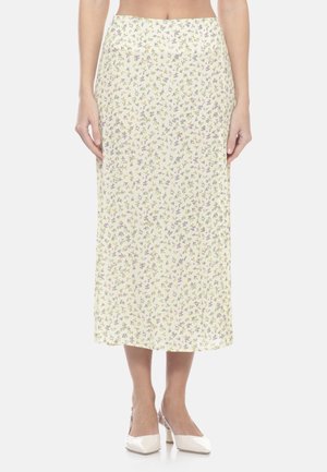 Femme portant une jupe crème taille haute, longue jusqu'aux chevilles, avec de petits motifs floraux violets et jaunes, associée à des talons blancs pointus.