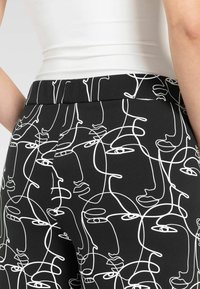 Pantaloni neri con un motivo astratto di volti bianchi, con una texture di tessuto liscia e una vita su misura.