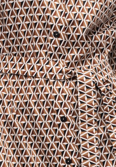 Ύφασμα με γεωμετρικό μοτίβο σε καφέ, λευκό και μαύρο χρώμα με ζώνη και μαύρα κουμπιά, εμφανίζεται σε κοντινή λεπτομέρεια.