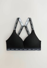 Zwarte bralette met kruisbanden en zwart-wit "NEXT" merkbranding. Zacht materiaal, driehoekige cups en een elastische band aan de onderkant.