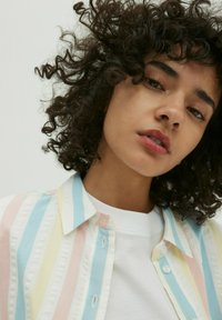 Kleurijk gestreept shirt in pastelkleuren van roze, blauw en geel; heeft een witte kraag en knopen, gecombineerd met een witte sweatshirt.