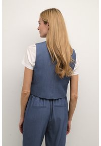 Blå chambray väst med en kortad design, bakdarts och en mjuk textur, bärs över en vit t-shirt, tillsammans med matchande byxor.