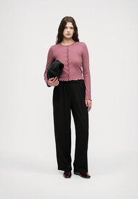 Haut à manches longues côtelé en rose doux avec fermeture à boutons, associé à un pantalon noir ample et un sac à main noir. Texture douce, coupe décontractée.