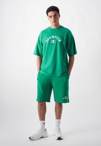 Grünes Baumwoll-T-Shirt und Shorts-Set mit einem weißen "CHAMPION"-Logo. Die Shorts haben Seitentaschen und ein gesticktes Logodetail.