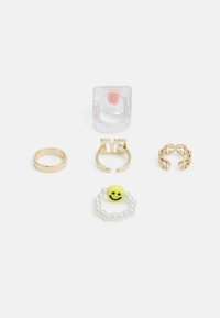 Cinco anéis: um anel transparente com uma flor, um anel dourado, um anel com detalhes em dourado, um anel aberto em dourado e um anel com contas com uma cara sorridente amarela.