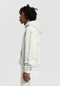 Ljusgrå hoodie i mjukt tyg, med en framficka, oversized passform och dragsko i huvan. Slät textur med ribbade manschetter.