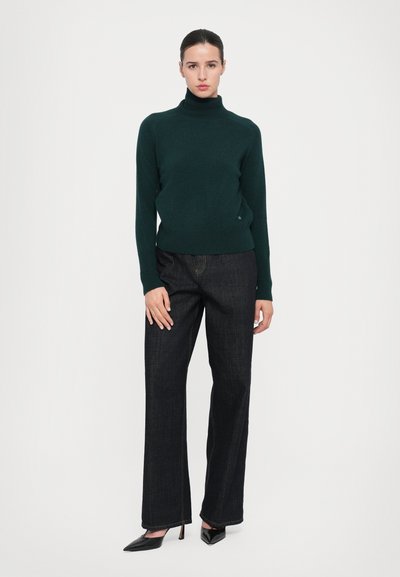 Donkergroene, gebreide turtlenecksweater gecombineerd met marineblauwe, wijdvallende denim broek en zwarte, puntige hakken. Eenvoudig ontwerp, getailleerde silhouet.