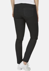 Svarta denimjeans med slim fit, med bakfickor och en slät yta. I kombination med vita sportskor.