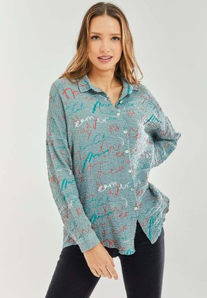 Light blue textured shirt with colorful scribble patterns in red and teal. Front buttons and a collared neckline, long sleeves.