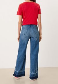 Rød kortærmet skjorte med afslappet pasform, parret med brede blå denimjeans, der har lommer og et let falmende i kanten.