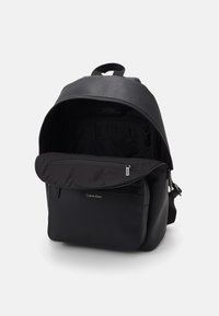 Zaino in pelle nera con una texture liscia, forma arrotondata, tasca frontale con zip e spallacci regolabili. L'interno è dotato di tasche organizzative.