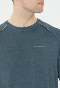 Mörkblå atletisk t-shirt med rundad halsringning, texturerad tyg och ljusgrå detaljer vid axelsömmarna. Har "ENDURANCE"-logotypen.