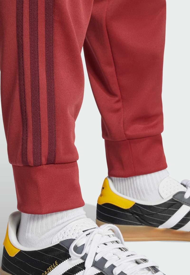 Red athletic pants with dark red stripes and elastic cuffs, paired with black and yellow sneakers featuring white accents and textured soles.