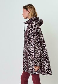 Kurtka w panterkę odporna na wodę z kapturem, o luźnym kroju, z zapięciem na sznurek i kontrastującymi ciemnymi akcentami.