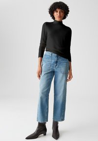 Schwarzes langärmeliges Rollkragenoberteil, kombiniert mit high-waisted blauen Denim-Jeans, die eine lockere Passform, gerade Beine und schwarze Stiefeletten aufweisen.