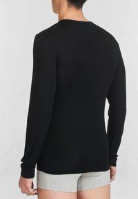 Maglietta nera a maniche lunghe realizzata in un tessuto leggero, con scollatura rotonda e silhouette aderente, vista da dietro.