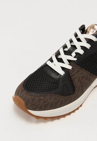 Baskets avec un dessus en maille marron et noire, des lacets blancs, une semelle en caoutchouc, des accents texturés et un capuchon lisse pour le confort et l'adhérence.