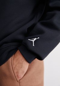 Felpa color navy con il logo Jumpman ricamato in bianco sul polsino, abbinata a pantaloni beige. Tessuto morbido con una vestibilità comoda.