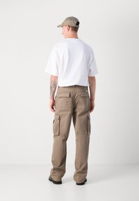 Beige cargo bukser med flere sidelommer, parret med en hvid t-shirt, set fra ryggen. Kasket i matchende beige farve.