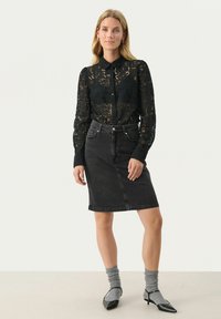 Zwarte kanten button-up blouse met lange mouwen, gecombineerd met een donkere denim kokerrok en grijze geribbelde sokken, gedragen met zwarte puntige hakken.