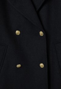 Cappotto doppiopetto in lana nera con bottoni dorati lucidi, tasche grandi e finitura strutturata. Design classico e sartoriale.